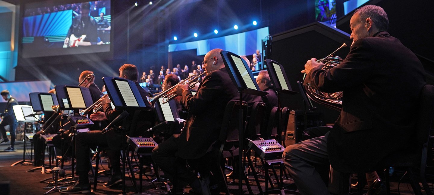 Musicians in the Prestonwood orchestra playing beneath blue stage lights
